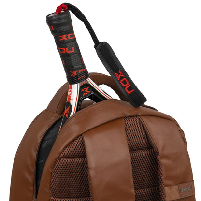 The NOX Pro Series Padel Backpack - Camel, with mesh straps and air ventilation, securely holds your padel racket—its handle wrapped in black and red NOX grip tape—making it ideal for carrying all your padel essentials.