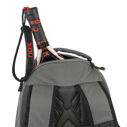 A close-up of the NOX Street Series Padel Backpack - Grey by NOX shows a partially unzipped top, revealing ergonomic padded straps and the handle and top of a black and red padel racket inside.