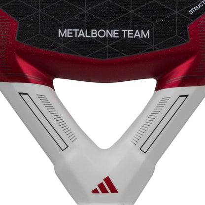 Close-up of the adidas Metalbone Team 3.3 Padel Racket, displaying "METALBONE TEAM" on a black-red background with a geometric pattern, Spin Blade Grit tech, and the red adidas logo on the white lower section.