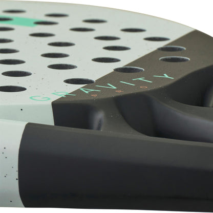 Close-up of the HEAD Gravity Pro 2024 Padel Racket by HEAD, featuring multiple round holes, a light grey surface, Spin Surface technology, and "GRAVITY" in green lettering near its black handle.