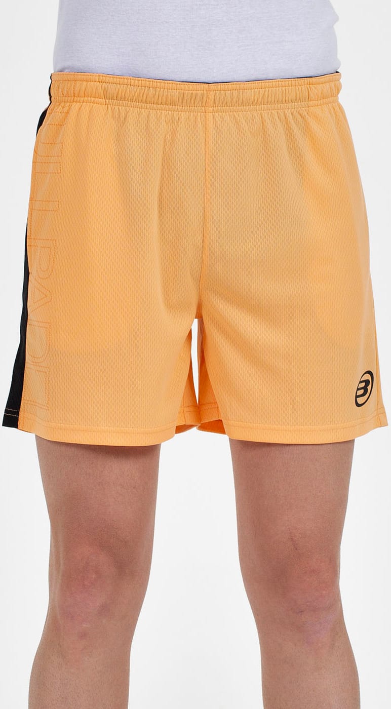A person wears Bullpadel Campaza Mens Padel Shorts in orange with a black vertical stripe and Tilllade logo on the left leg, featuring QuickerDry technology. Only the shorts and part of the legs are visible against a plain white background.