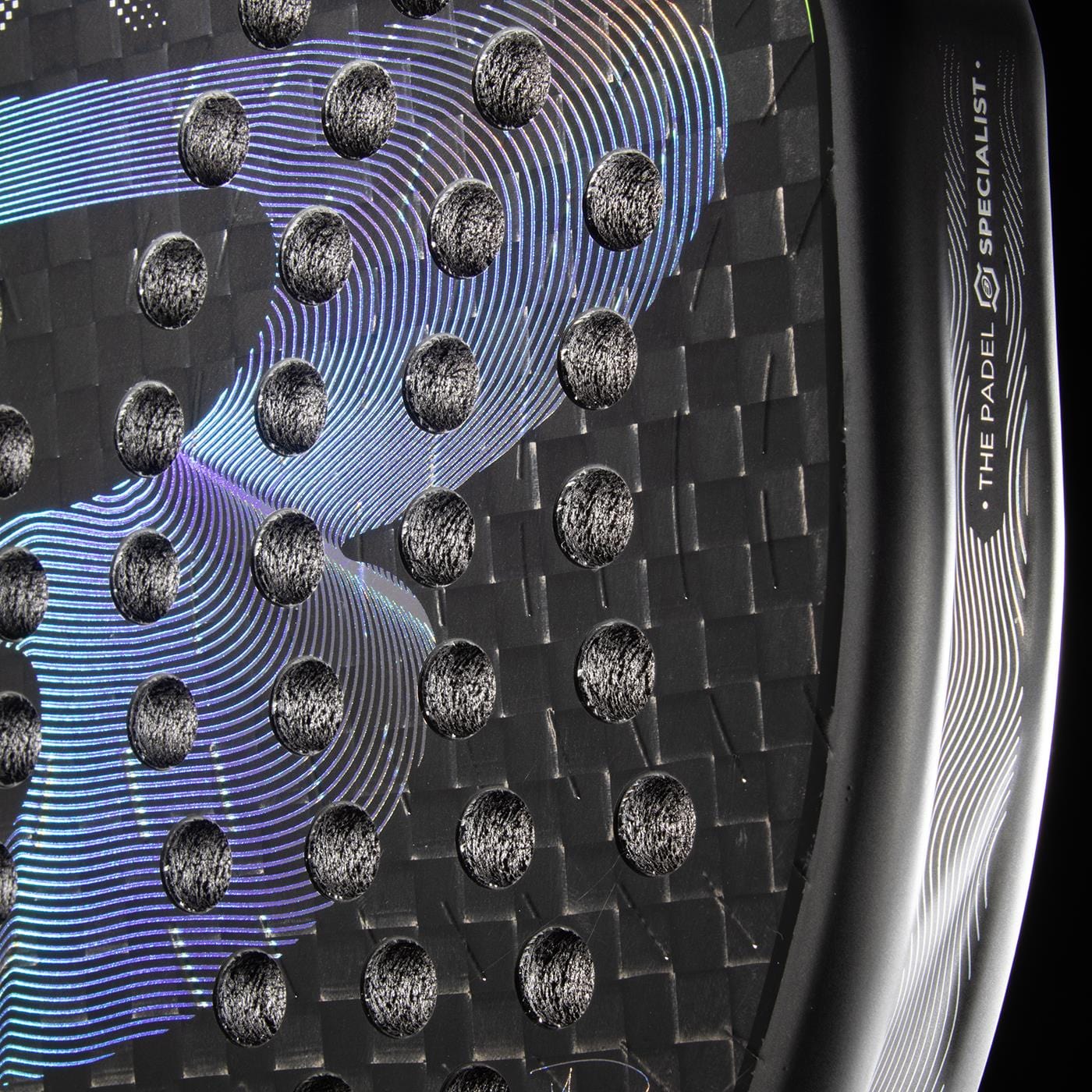 Close-up of the Bullpadel XPLO 2026 Padel Racket by Bullpadel, featuring a black textured carbon fiber surface with circular holes and iridescent curves. "THE PADEL SPECIALIST" is displayed on the rim of this powerful racket.