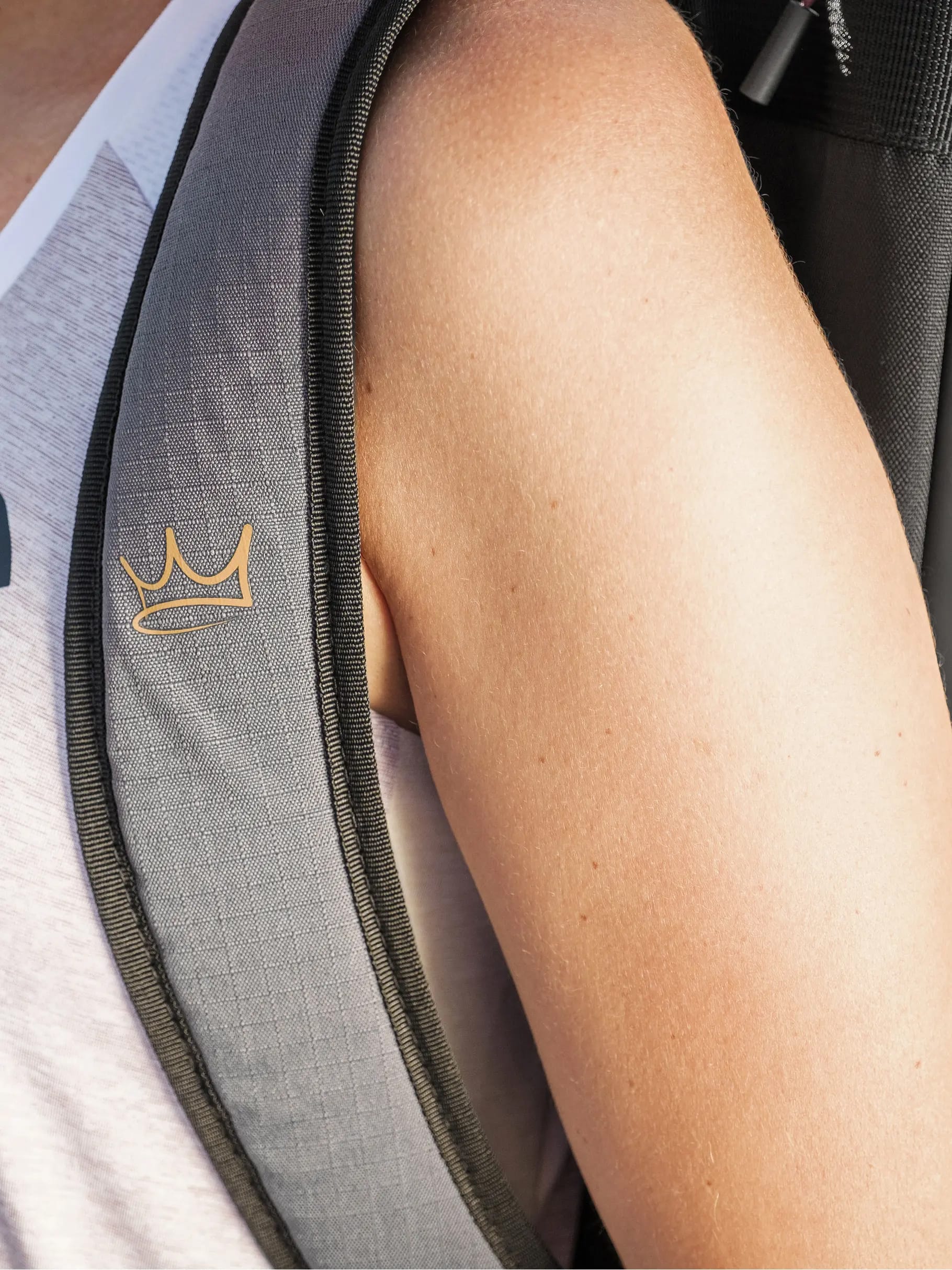 Close-up of a person's shoulder wearing a sleeveless white top and the gray strap of the HEAD Tour Padel Racket Bag L - Coello by HEAD, featuring a small gold crown logo. The image highlights the stylish strap, ideal for carrying your padel racket bag.