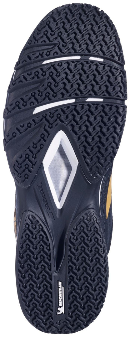 The image shows the black rubber sole of Babolat Premura 3 Mens Padel Shoes - Black / Gold, featuring zigzag and diamond tread patterns for grip, white and yellow accents, and a prominent Michelin logo near the heel.