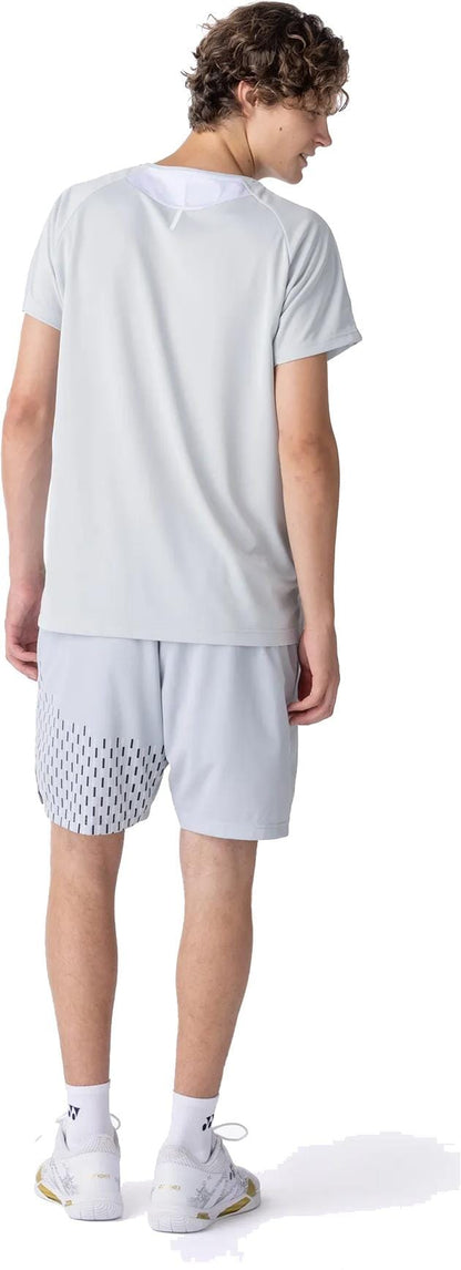 A person with curly hair wears a Yonex 10713EX Crew Neck Men's Padel T-Shirt in Silver Grey, patterned light gray shorts, white socks, and white sneakers, standing and facing away from the camera.