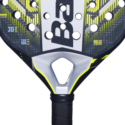 Close-up of the Babolat Counter Veron 2.5 Padel Racket head, featuring a black, gray, and yellow design with holes and Carbon Flex technology. The black handle has a textured grip and displays the “Babolat” brand name.