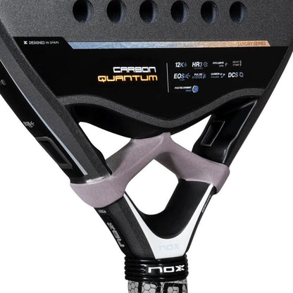 Close-up of the NOX Luxury Quantum 12K Carbon 2025 Padel Racket, highlighting EXCLUSIVE SPIN technology and technical specs on its black 12K carbon fiber surface, with focus on the handle and throat area.