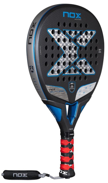 The NOX NFA Future Hybrid 12K Alum Padel Racket by NOX features a black, blue, and gray design with a large center "X," circular holes on the face, and a red and black grip with an attached wrist strap.