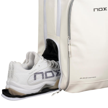 A pair of white NOX athletic shoes is partially tucked into a white NOX Pro Series Padel Backpack with a side zipper compartment; both feature "nox" branding.