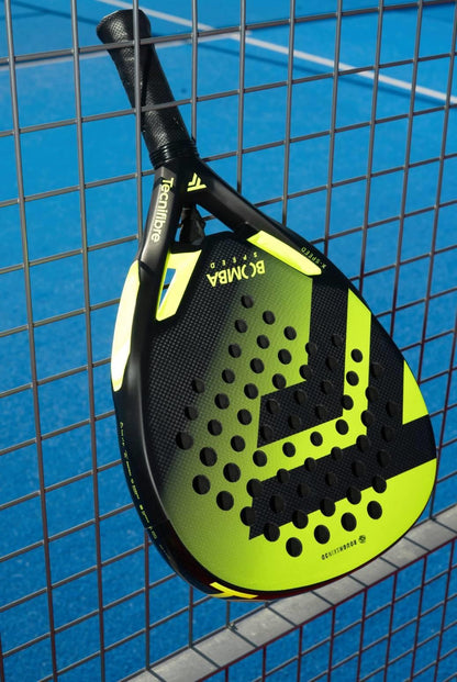 A black and yellow Tecnifibre Bomba Speed Padel Racket with a geometric design hangs on a blue padel court fence, highlighting its offensive capabilities.