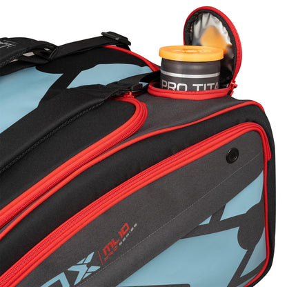 A close-up of a NOX ML10 Team Padel Racket Bag - Black / Clay with red zippers and a blue and black design. The open side pocket reveals an orange water bottle marked "PRO TITAN.