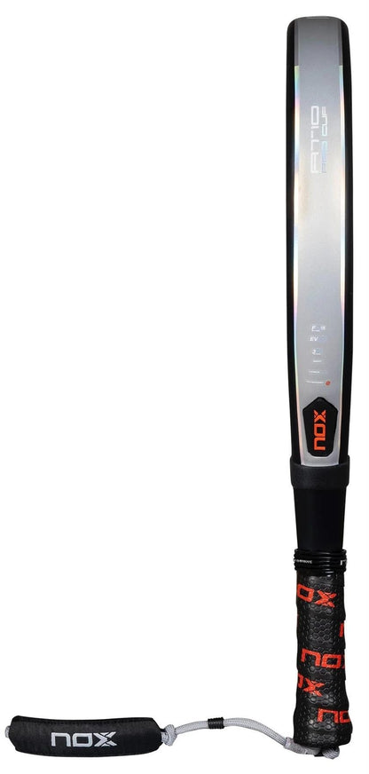 The NOX AT10 Pro Cup HARD By Agustin Tapia 2025 padel racket features a striking black and silver design with red accents, a black handle with branded grip tape, and a Smartstrap® wrist strap displaying the NOX logo.