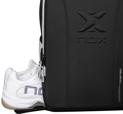 A close-up of the NOX Luxury Master Series Padel Backpack - Black / White shows its zippered compartment partially open with white athletic shoes inside, and the NOX logo embossed on the sleek front panel.