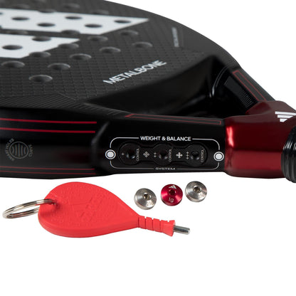 Close-up of the adidas Metalbone 3.3 Padel Racket, which features a Weight & Balance adjustment system, two removable weights, an adjustment tool, and a keychain in front of the adjustable racket.